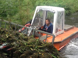 De bestuurder van de maaiboot dumpt het opgehaalde groen langs de kant. 