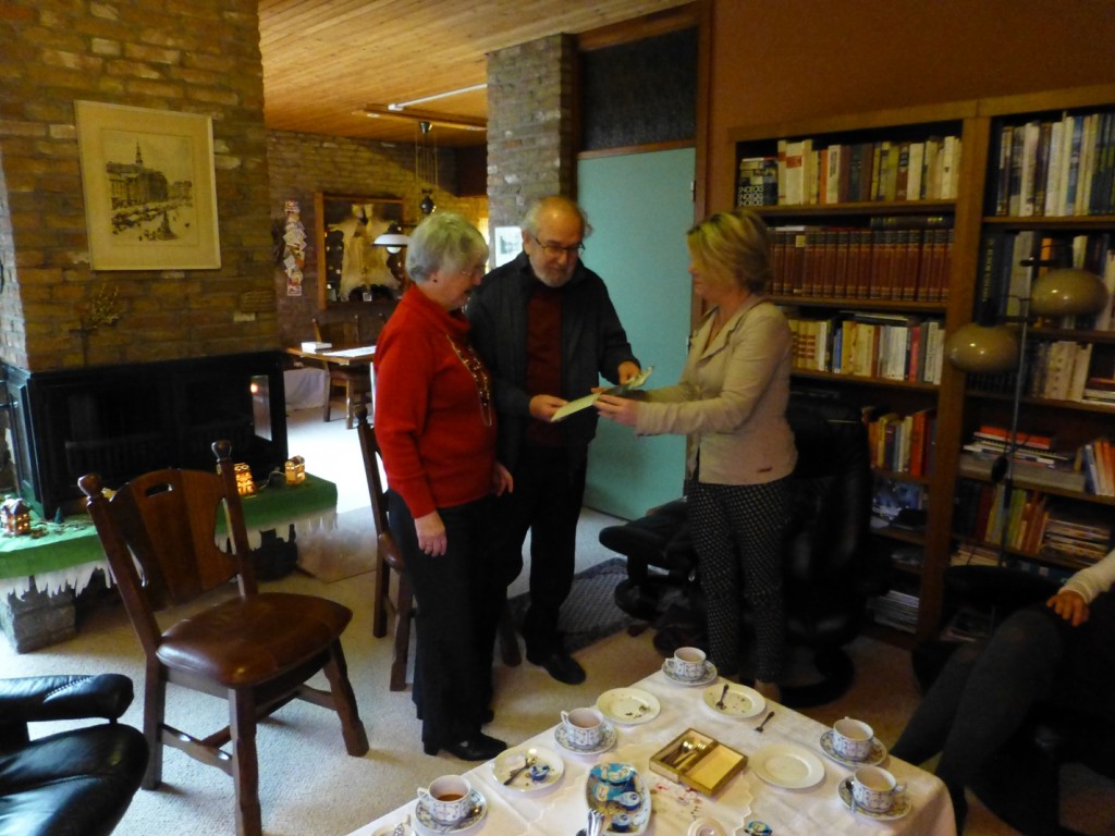 Leo en Riet Teulings nemen in hun huis aan de Tweede Hervendreef het eerste exemplaar van de jubileumkrant in ontvangst uit handen van voorzitter Marlies Pulsford van de wijkvereniging.