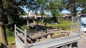 Delen van de oude brug, waarvan sommige rot, liggen klaar om afgevoerd te worden.
